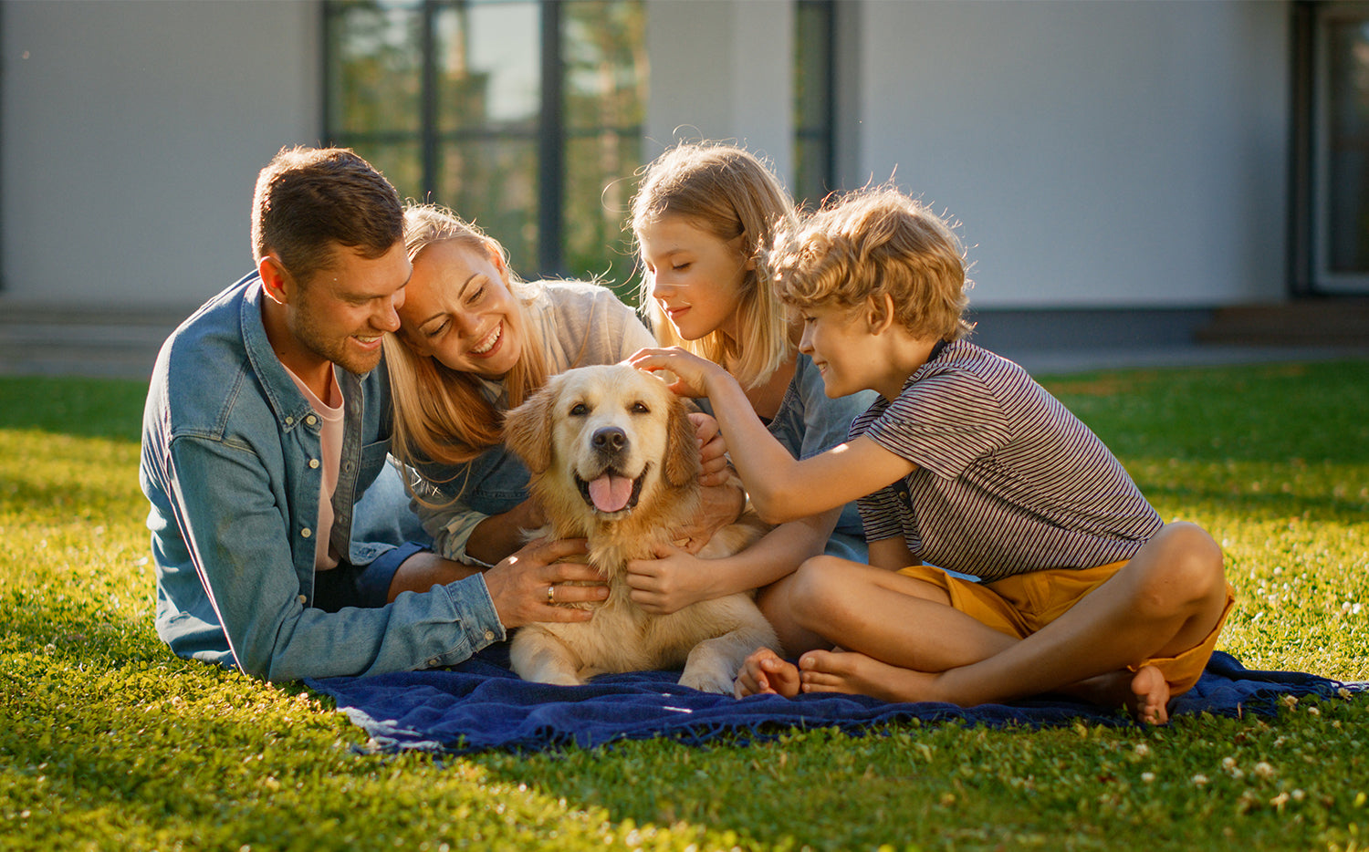 A family of four sitting on the lawn with their golden retriever.